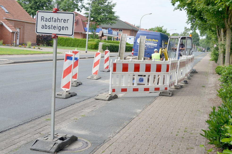 Aktuell ist die Friedhofstraße in Ramsloh für den motorisierten Verkehr nutzbar. Nur Radfahrer müssen absteigen, weil Mitarbeiter der Strücklinger Firma Schulte-Perk im Auftrag der Gemeinde Bordsteinabsenkungen entfernen. Nächste Woche wird die Straße aber schon wieder voll gesperrt. Foto: Fertig