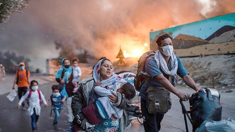 Migranten fliehen vor einem großen Feuer mit ihren Habseligkeiten aus dem Flüchtlingslager Moria. Foto: Petros Giannakouris/AP/dpa