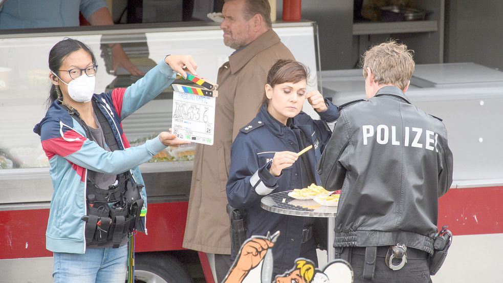 An einer Fischbude am Hafen in Weener schaut Kommissar Jan Brockhorst (Felix Vörtler) wie üblich mürrisch, während die Streifenpolizisten Süher Özlügül (Sophie Dal) und Henk Cassens (Maxim Mehmet) sich Pommes frites schmecken lassen. Foto: Bruins