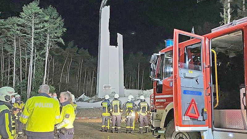 Feuerwehrleute und Polizisten stehen vor den Resten des Turms der Windenergieanlage. Foto: Guido Bludau/Foto Bludau/dpa