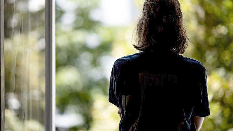 Eine Frau steht in ihrer Wohnung an einem Fenster. (Archivbild). Foto: Fabian Sommer/dpa