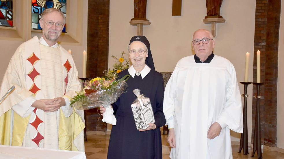 Pfarrer Ludger Fischer (links) und Pfarreiratsvorsitzender Georg Pugge (rechts) beglückwünschten Schwester Elsmarie mit einem Blumenstrauß und einem Präsent. Foto: Hellmann