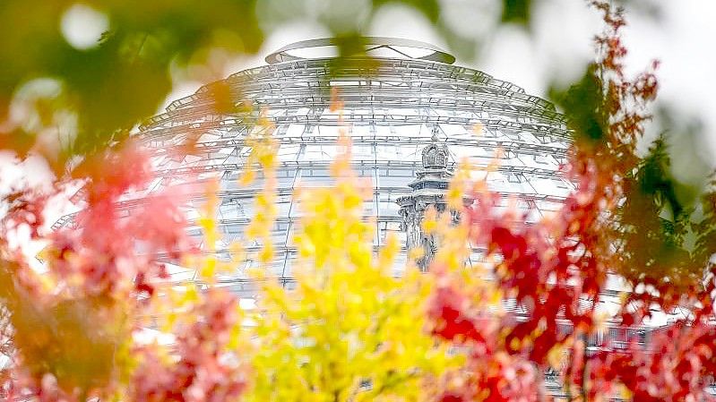 Rot-gelb-grün herbstlich verfärbte Blätter sind an Bäumen vor der Reichstagskuppel zu sehen. Foto: Britta Pedersen/dpa-Zentralbild/dpa