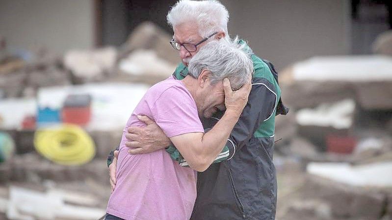 Weinend liegen sich die Brüder Bernd (l) und Gerd Gasper vor ihrem von der Flut zerstörten Elternhaus in Altenahr in den Armen. Foto: Boris Roessler/dpa