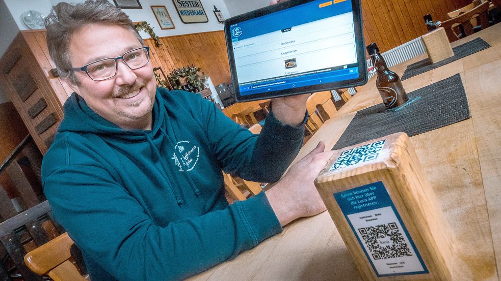 Brauhaus-Chef René Krischer zeigt eins der 40 Tablets, die er angeschafft hat. Über den QR-Code auf dem Holzwürfel können Gäste ihre Geräte anmelden und Bestellungen abgeben. Über den Luca-App-Code können sie zudem einchecken. Foto: Cordsen