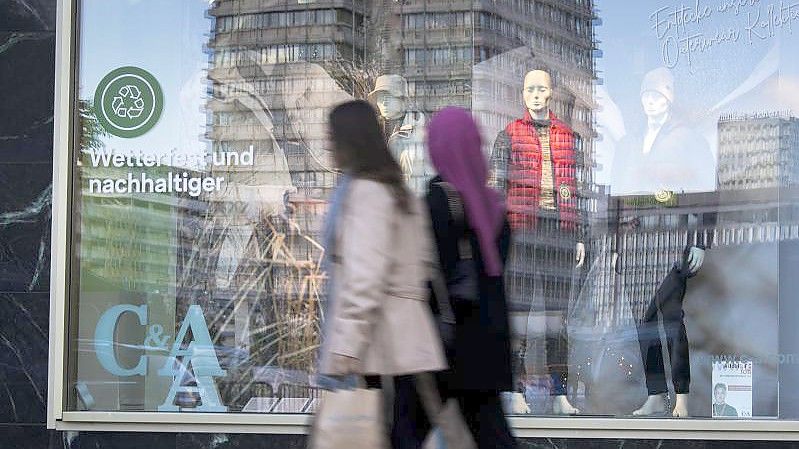 Passanten gehen an einem Schaufenster am Berliner Alexanderplatz vorbei. Foto: Carsten Koall/dpa