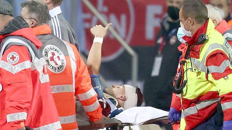 Der Nürnberger Tom Krauß (M) wird verletzt aus dem Stadion getragen, zeigt aber mit dem Daumen nach oben. Foto: Daniel Karmann/dpa