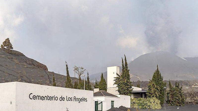 Der Friedhof von Los Angeles ist mit Asche bedeckt, während im Hintergrund die Rauch- und Aschesäule zu sehen ist, die der Vulkan Cumbre Vieja ausstößt. Foto: Europa Press/EUROPA PRESS/dpa