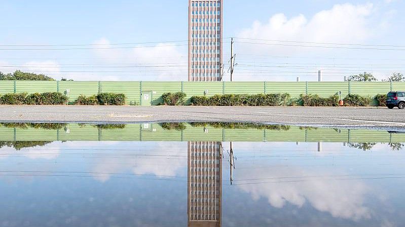 Das Markenhochhaus vom Volkswagen spiegelt sich in einer Pfütze auf einem Mitarbeiterparkplatz vor dem VW Werk Wolfsburg. (Archivbild). Foto: Julian Stratenschulte/dpa