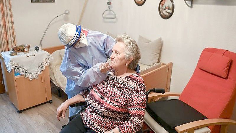 Die Krankenschwester eines mobilen Test-Teams des Deutschen Roten Kreuzes (DRK) testet in einer DRK-Seniorenbetreuungseinrichtung in Brandenburg eine Seniorin. Foto: Jens Kalaene/dpa-Zentralbidl/dpa