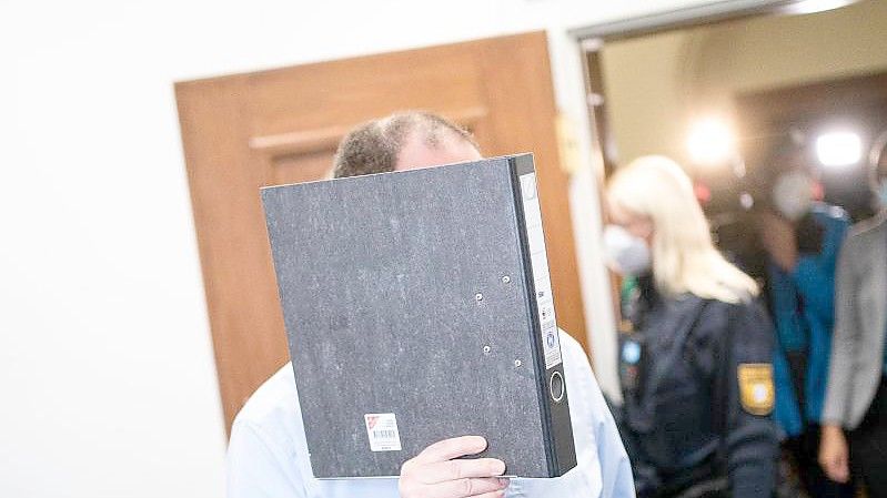 Der Angeklagte versteckt sein Gesicht beim Prozessauftakt hinter einem Ordner. Foto: Nicolas Armer/dpa