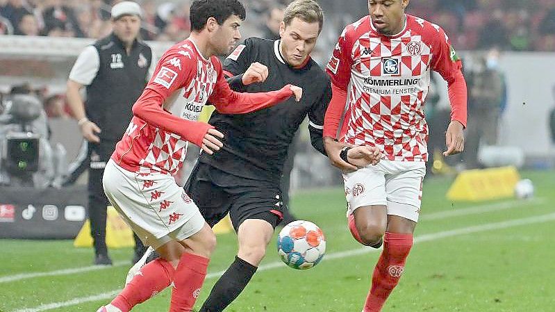 Die Mainzer Aaron Martin (l.) und Jean-Paul Boetius versuchen Kölns Benno Schmitz vom Ball zu trennen. Foto: Torsten Silz/dpa