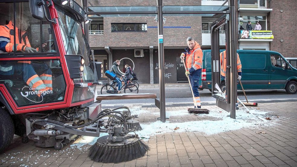 Am Montag waren Mitarbeiter der Gemeinde Groningen damit beschäftigt, die Scherben an dem Bushäuschen aufzukehren, das in der Nacht zuvor zerstört worden war. Foto: Sparidaens/ANP/DPA