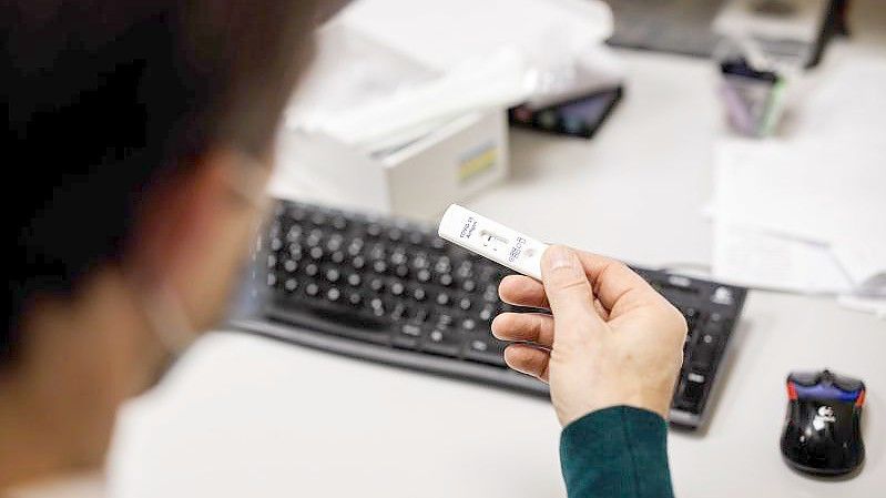 Ein Mitarbeiter blickt auf das Testergebnis für einen Corona-Schnelltest eines anderen Mitarbeiters. Foto: Matthias Balk/dpa