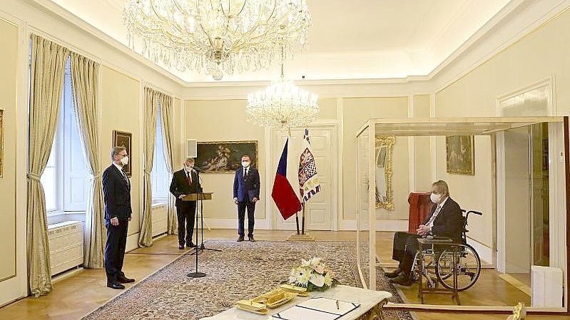 Der tschechische Präsident Milos Zeman (r) sitzt während der Vereidigung von Petr Fiala (l) in einem Rollstuhl hinter einer durchsichtigen Wand. Foto: Roman Vondrous/CTK/AP/dpa