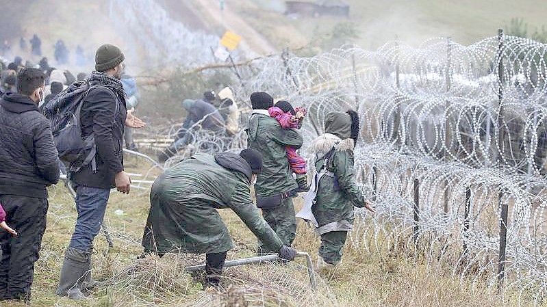 Getrennt durch Stacheldraht: Migranten stehen an der Grenze auf der belarussischen Seite - auf der polnischen stehen Sicherheitskräfte. Foto: Leonid Shcheglov/BelTA/AP/dpa