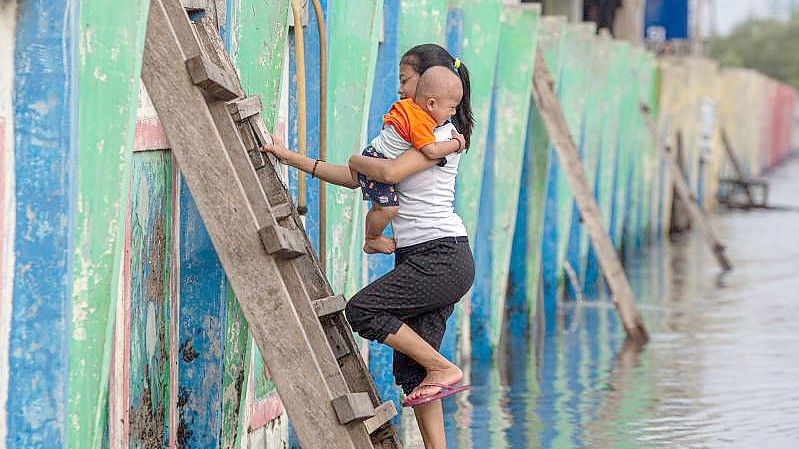 Eine Frau, die ein Baby hält, klettert an der Küste von Jakarta auf einer Leiter aus dem Flutwasser. Foto: Afriadi Hikmal/XinHua/dpa