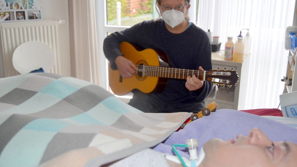 Musiktherapeut Manfred Lüsing-Hauert spielt auf der Gitarre für einen dauerbeatmeten Patienten der FIP. Musik soll Abwechslung und Freude in den Alltag der FIP-Bewohner bringen. Foto: Fertig