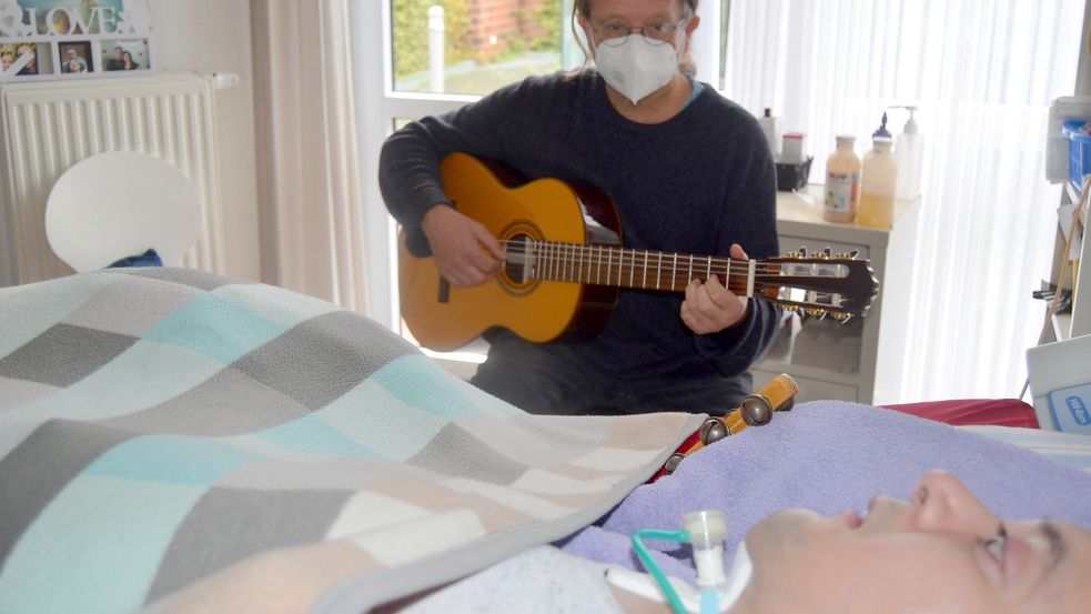 Musiktherapeut Manfred Lüsing-Hauert spielt auf der Gitarre für einen dauerbeatmeten Patienten der FIP. Musik soll Abwechslung und Freude in den Alltag der FIP-Bewohner bringen. Foto: Fertig