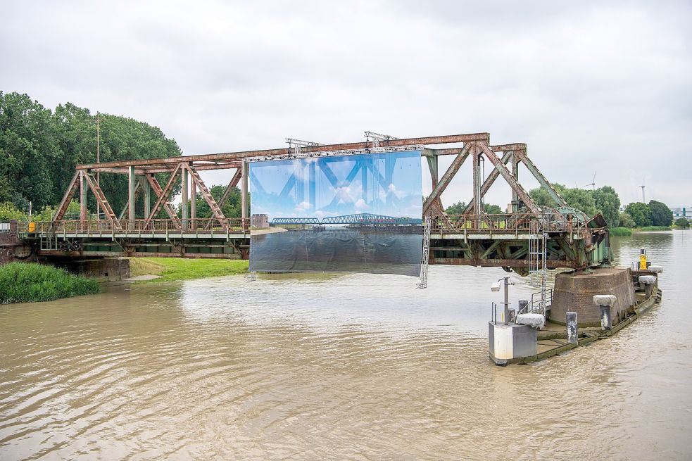 Ein Plakat mit einer Darstellung der geplanten Brücke hängt an der alten Friesenbrücke über der Ems. Foto: Schuldt/DPA