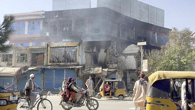 Menschen fahren in Kundus an Trümmern von Geschäften vorbei, die bei Zusammenstößen zwischen den Taliban und afghanischen Sicherheitskräften zerstört wurden. Foto: Abdullah Sahil/AP/dpa/Archiv
