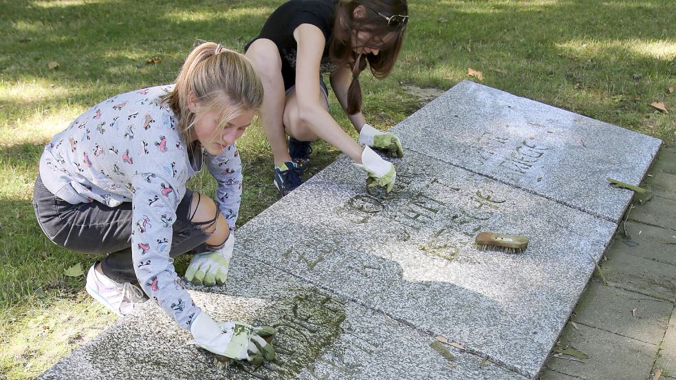 Zwei junge Frauen aus Weißrussland reinigen auf dem Soldatenfriedhof in Wismar (Mecklenburg-Vorpommern) einen Gedenkstein bei einem Arbeitseinsatz des Internationalen Workcamps Versöhnung über den Gräbern - Arbeit für den Frieden" des Landesverbandes des Volksbundes Deutsche Kriegsgräberfürsorge. Foto: Wüstneck/DPA