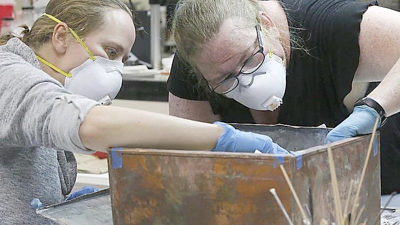 Sue Donovan (l) und Kate Ridgeway untersuchen die Artefakte der Zeitkapsel. Foto: Bob Brown/Richmond Times-Dispatch/AP/dpa