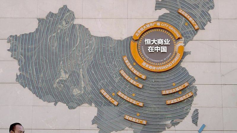 Eine Aufsichtsperson steht neben einer Karte in Peking, auf der die Evergrande-Entwicklungsprojekte abgebildet sind. Foto: Andy Wong/AP/dpa