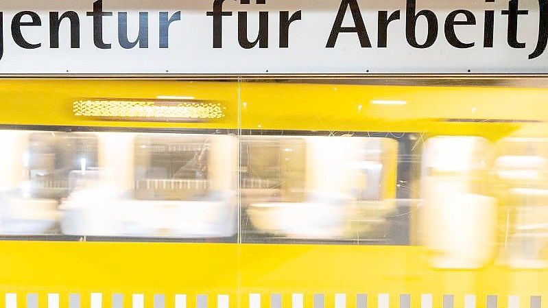 Der Schriftzug "„Agentur für Arbeit“" steht am frühen Morgen an einer Stuttgarter Haltestelle geschrieben, während im Hintergrund eine Stadtbahn einfährt. Foto: Christoph Schmidt/dpa
