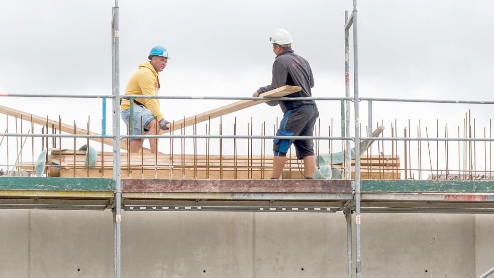 Die Baubranche hat Hochkonjunktur. Hier heben zwei Bauarbeiter auf einer Baustelle auf einem Hausdach ein Brett. Foto: Riechau/DPA