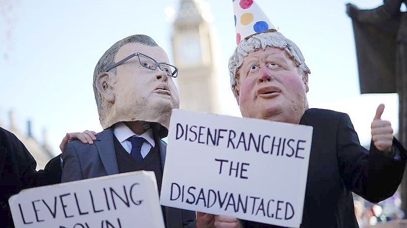 Zwei Demonstranten in Westminster haben sich als Minister Michael Gove und Premier Boris Johnson verkleidet - letzterer mit Partyhütchen. Foto: Aaron Chown/PA Wire/dpa