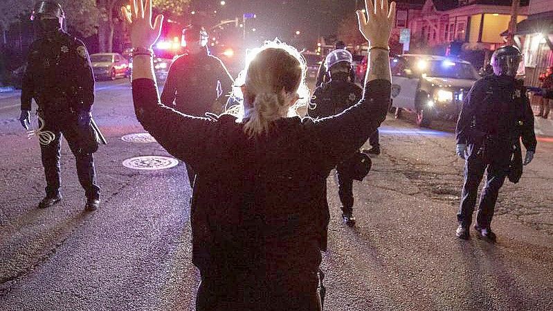 Eine Demonstrantin steht bei einem Protest gegen Polizeigewalt in Oakland mit hochgestreckten Armen vor Polizisten. Foto: Ethan Swope/AP/dpa