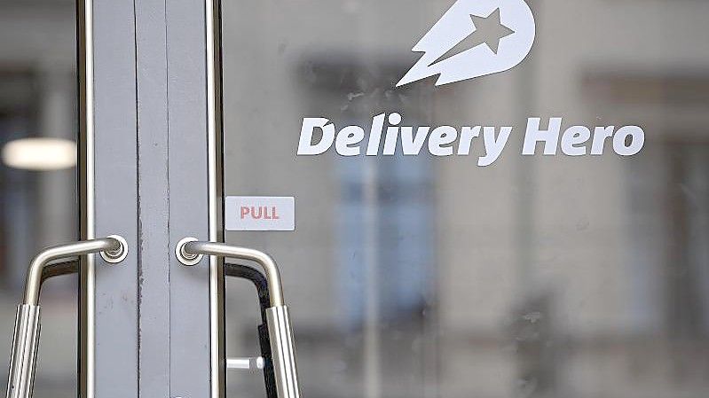 Das Logo Essenslieferdienstes Delivery Hero ist an einer Glasscheibe der Zentrale angebracht. Der Lieferdienst blickt vor allem auf den Weltmarkt. Übernahmen und Investitionen sorgen für schnelles Wachstum bei hohen Verlusten. Foto: Britta Pedersen/dpa-Zentralbild/dpa