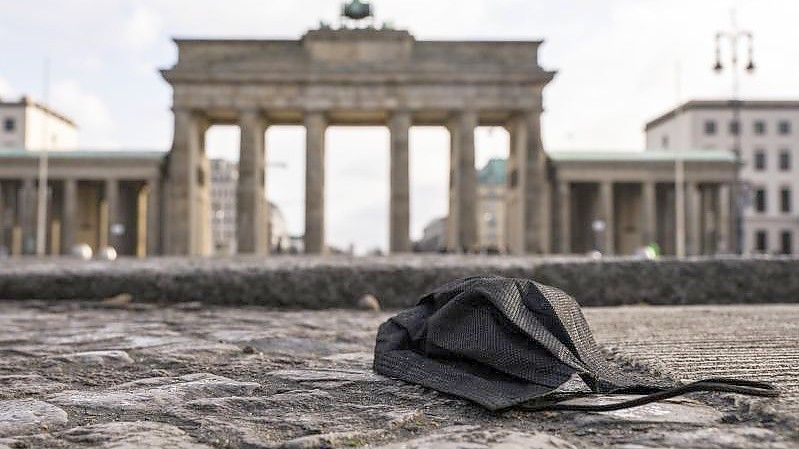 Eine schwarze Corona-Makse liegt auf dem Boden vor dem Brandenburger Tor. Foto: Christophe Gateau/dpa