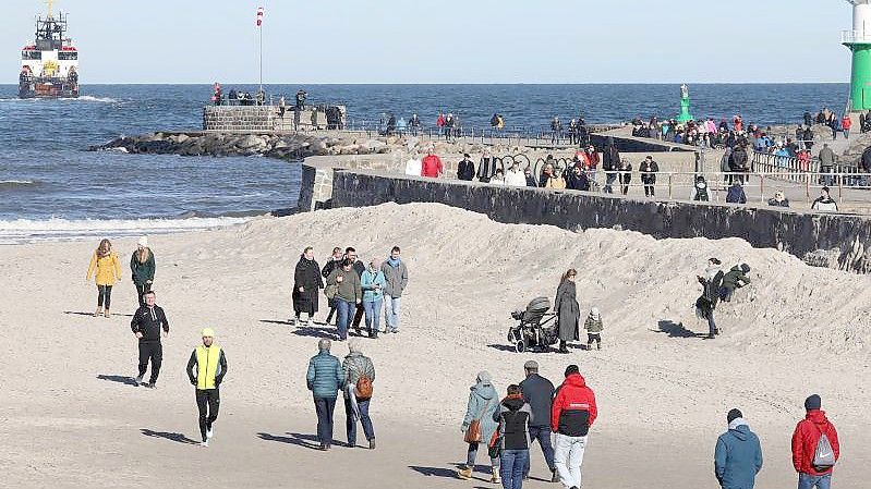 Spaziergänger genießen am Ostseestrand in Warnemünde das sonnige Wetter. Foto: Bernd Wüstneck/dpa-Zentralbild/dpa