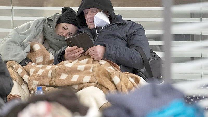 Zwischen Reisetaschen sitzend warten aus der Ukraine geflüchtete Menschen am Sonntagmorgen am Berliner Hauptbahnhof auf ihre Weiterreise. Foto: Paul Zinken/dpa