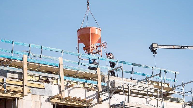 Arbeiter leeren auf einer Baustelle eines Neubaus einen Behälter für Beton. Foto: Daniel Bockwoldt/dpa