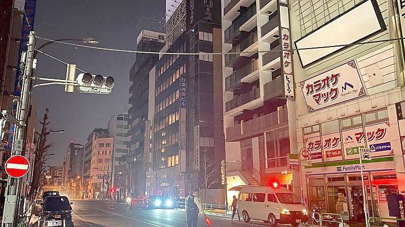 Ein Polizist steht während eines Stromausfalls in Tokio auf der Straße und leitet den Verkehr. Foto: -/Kyodo News/AP/dpa