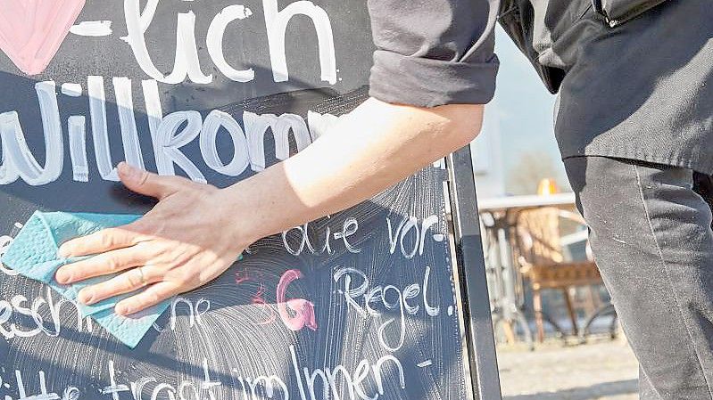 Kellner Tonet Devolli vom Restaurant Mühlstein in Wedel beseitigt die Hinweise zu den 3G-Regeln. Foto: Georg Wendt/dpa