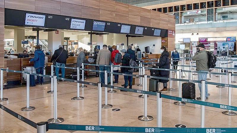 Reisende stehen am BER an einem Check-in Schalter. Foto: Paul Zinken/dpa