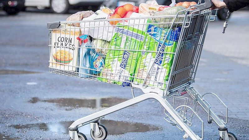 Ein Kunde schiebt einen bis zum Rand gefüllten Einkaufswagen über den Parkplatz eines Supermarktes. Foto: Matthias Balk/dpa