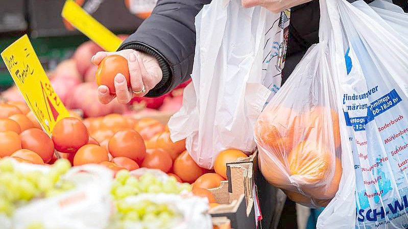 Eine Kundin begutachtet eine Tomate auf einem Wochenmarkt in Hannover. Wegen der steigenden Inflation müssen viele Menschen in Deutschland den Gürtel enger schnallen,. Foto: Moritz Frankenberg/dpa