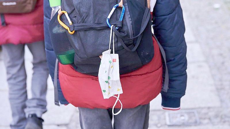 Eine Kindermaske hängt an einem Rucksack eines Schulkindes. Ab Montag fällt die Maskenpflicht in allen Jahrgängen weg. Foto: Annette Riedl/dpa