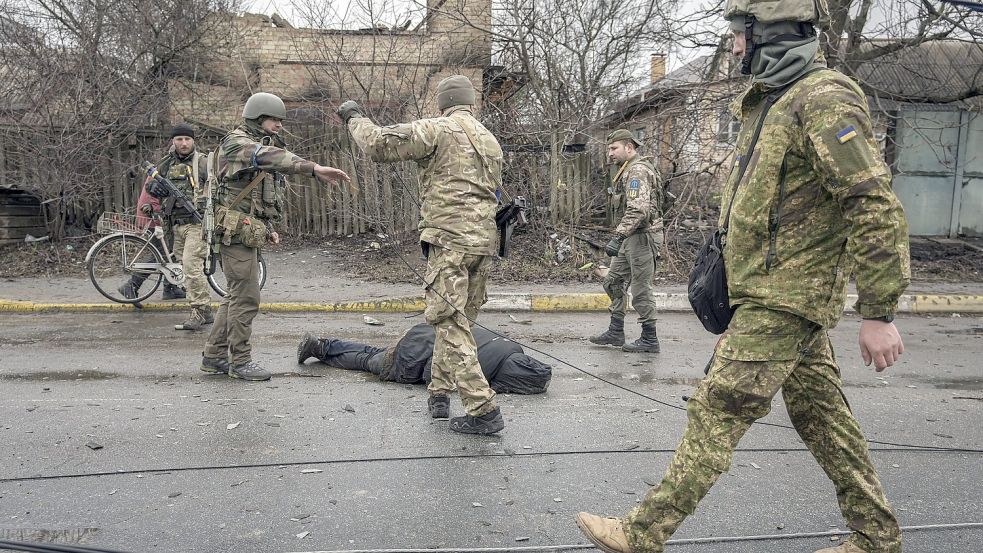 Ukrainische Soldaten befestigen ein Kabel an der Leiche eines Zivilisten, während sie in dem ehemals russisch besetzten Kiewer Vorort Butscha nach Sprengfallen suchen. Der ukrainische Präsident Selenskyj sagte, dass die russischen Truppen Minen, Ausrüstung und sogar Leichen zurücklassen. Foto: Vadim Ghirda/AP/DPA