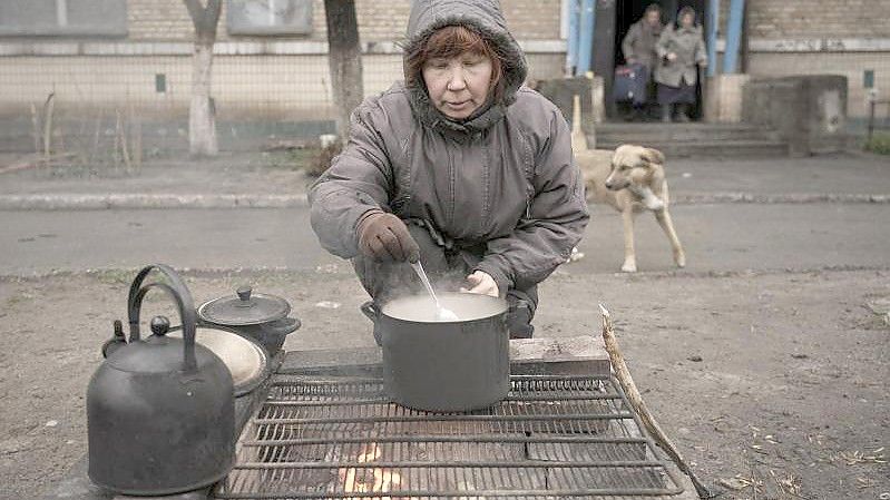 Eine Frau kocht auf einem offenen Feuer vor einem Wohnhaus in Butscha. Foto: Vadim Ghirda/AP/dpa