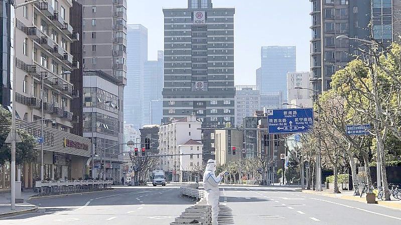 Ein Mann in einem Schutzanzug steht inmitten leerer Straßen in einem abgesperrten Gebiet im Bezirk Jingan im Westen von Shanghai. Foto: Chen Si/AP/dpa