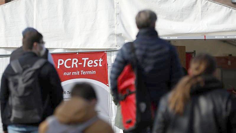 Menschen stehen für einen PCR-Test in einer Teststation am Lübecker Holstentor Schlange. Foto: Christian Charisius/dpa