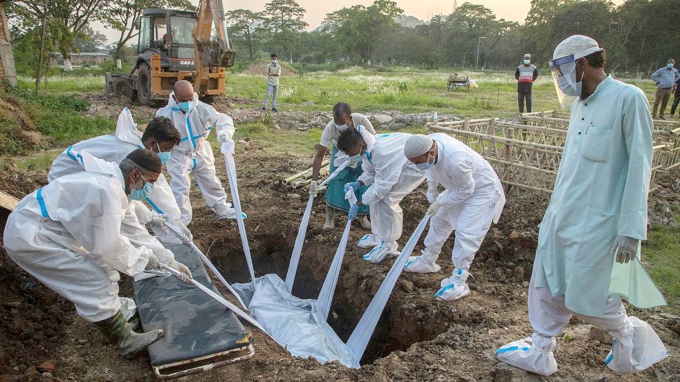 Angehörige und städtische Mitarbeiter in Schutzanzügen begraben in Indien den Körper einer Person, die an Covid-19 gestorben ist. Foto: Anupam Nath/AP/dpa