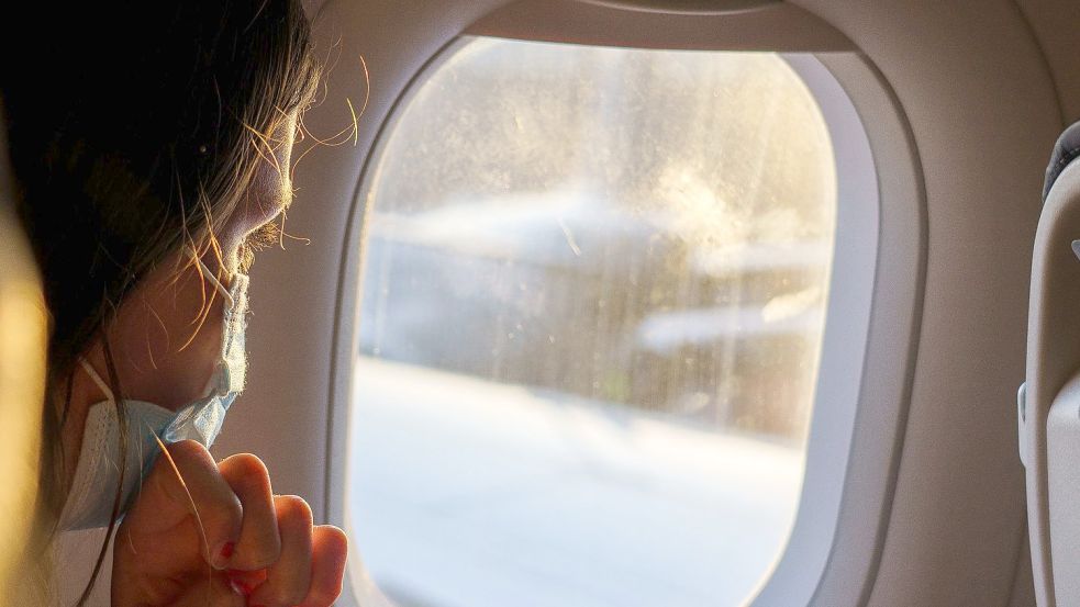 Ein weiblicher Fluggast mit Maske schaut vor dem Start aus dem Fenster. Auf Flügen von und nach Deutschland muss weiter Maske getragen werden. Foto: Andreas Arnold/dpa