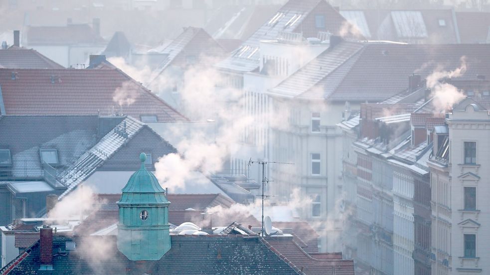 Rauch strömt aus Kaminen auf Dächern von Mehrfamilienhäuser. Foto: Jan Woitas/dpa